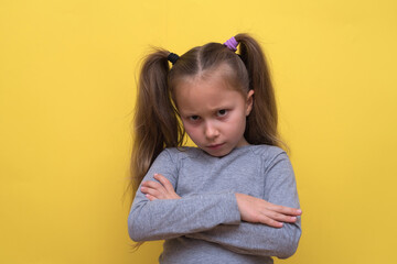 A cute girl in a gray T-shirt shows emotions on a yellow background.