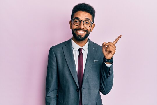 Handsome hispanic business man with beard wearing business suit and tie with a big smile on face, pointing with hand and finger to the side looking at the camera.