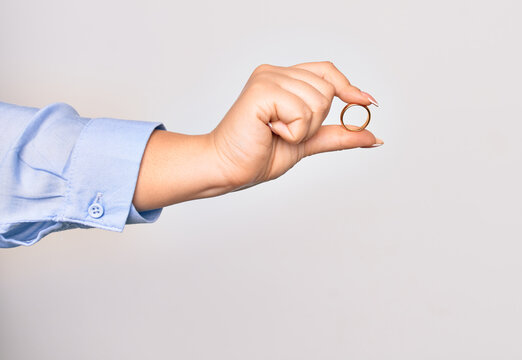 Hand of caucasian young woman holding golden marriage ring over isolated white background