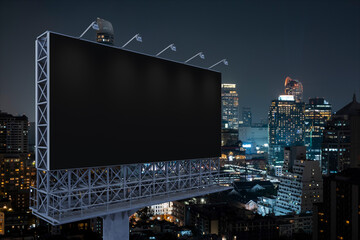 Blank black road billboard with Bangkok cityscape background at night time. Street advertising poster, mock up, 3D rendering. Side view. The concept of marketing communication to promote idea.