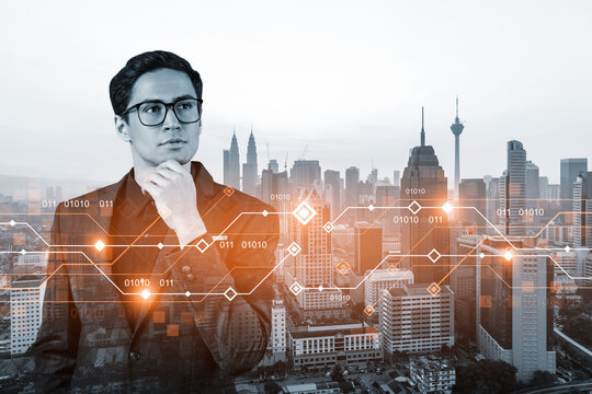 Eastern young businessman pondering on technology at business process to achieve tremendous growth. Worldwide process to conduct transactions. Tech hologram icons over Kuala Lumpur background