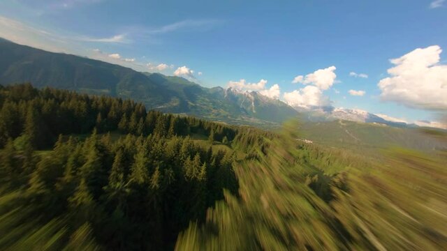 A dynamic FPV drone shot through some pine trees above a young couple, revealing a gorgeous backdrop over the Vall&eacute;e du giffre in the French Alps