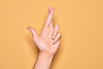 Hand of caucasian young man showing fingers over isolated yellow background gesturing fingers crossed, superstition and lucky gesture, lucky and hope expression - obrazy, fototapety, plakaty