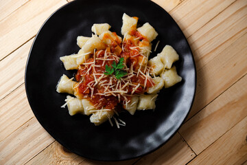 gourmet potato gnocchi with tomato sauce and parmesan seen from above on black plate and wooden table