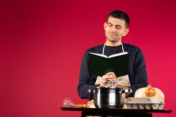 A male cook in the kitchen reads book with recipes. Pink background and side space for advertisment