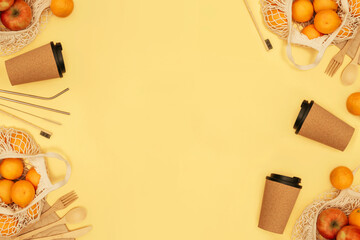 Reusable wooden cutlery, cork mug and grocery bag with fruits. Toothbrush and juice tube with brush, eco friendly fork, knife, spoon and stics on yellow background. Zero waste concept. Copyspace.