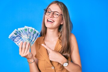 Young blonde girl holding south african rand banknotes winking looking at the camera with sexy...