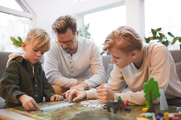 Portrait of loving father spending time with two sons playing board games and puzzles together in modern home interior