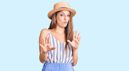 Young beautiful blonde woman wearing summer hat moving away hands palms showing refusal and denial with afraid and disgusting expression. stop and forbidden.