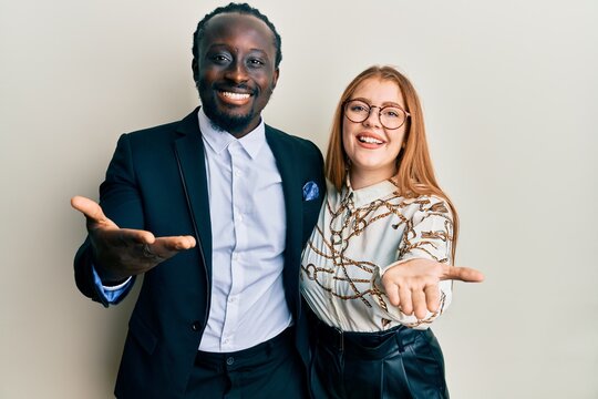 Young interracial couple wearing business and elegant clothes smiling cheerful offering palm hand giving assistance and acceptance.