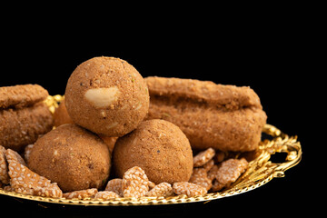 Indian Dessert Gud Til Ke Khasta Gol Gazak Laddu Gajak Rolls Stacked In Golden Designer Tray On Isolated Black Background. Sweets Mostly Consumed In Winters That Keeps Body Warm And Prevent From Cold