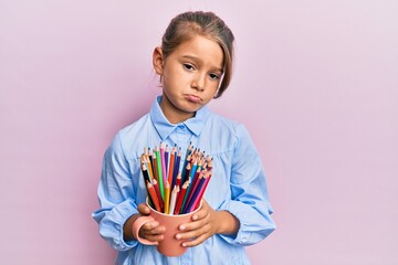 Little beautiful girl holding colored pencils depressed and worry for distress, crying angry and...