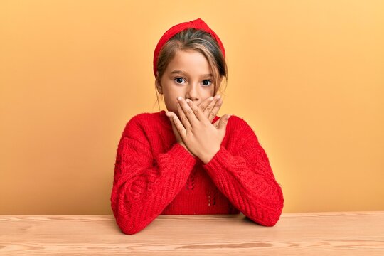 Little beautiful girl wearing casual clothes sitting on the table shocked covering mouth with hands for mistake. secret concept.