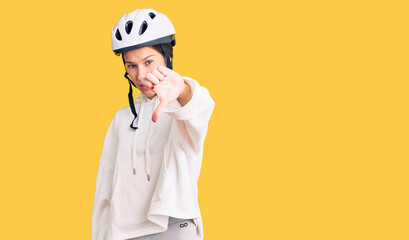 Beautiful brunette young woman wearing bike helmet and sporty clothes looking unhappy and angry showing rejection and negative with thumbs down gesture. bad expression.