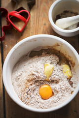 Gingerbread cookie ingredients in white bowl: eggs, spices, flour, egg