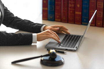 Female hands with a judge's gavel in front of a laptop monitor. - obrazy, fototapety, plakaty
