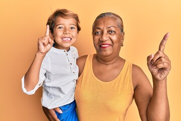 Hispanic grandson and grandmother together over yellow background smiling with an idea or question...