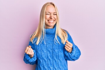 Young blonde girl wearing wool winter sweater excited for success with arms raised and eyes closed celebrating victory smiling. winner concept.