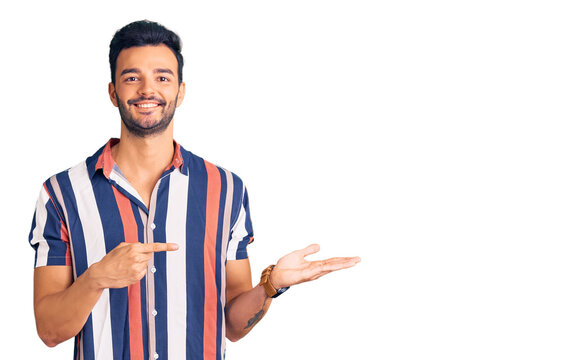 Young handsome hispanic man wearing casual  summer shirt amazed and smiling to the camera while presenting with hand and pointing with finger.