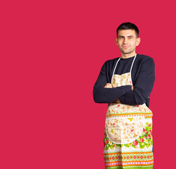 Young man in a kitchen apron on pink background with blank space. The concept of gender stereotypes.
