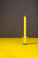 Yellow tall candle in a glass candlestick, trendy colors of the year, yellow and gray background