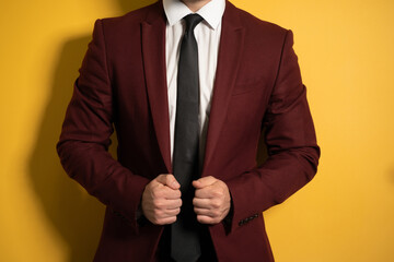 No head close up shot pf a hands holding a business man burgundy color jacket with two hands fixing it on a body isolated on yellow background. 