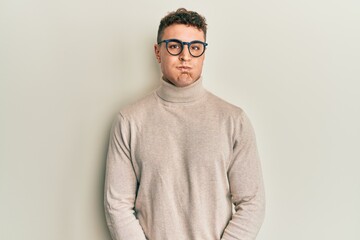 Fototapeta premium Hispanic young man wearing casual turtleneck sweater puffing cheeks with funny face. mouth inflated with air, crazy expression.