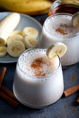 Banana smoothie with cinnamon in glasses with fruits on stone background.