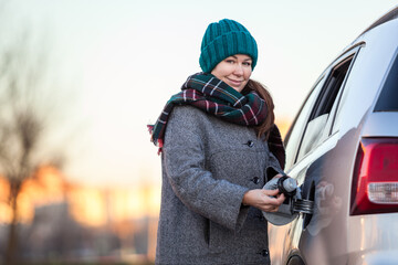 Positive Caucasian female driver portrait with opened gas cap lid of her car, looking at camera