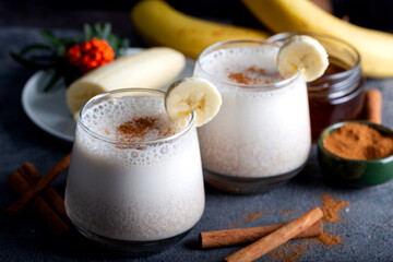 Banana smoothie with cinnamon in glasses with fruits on stone background.