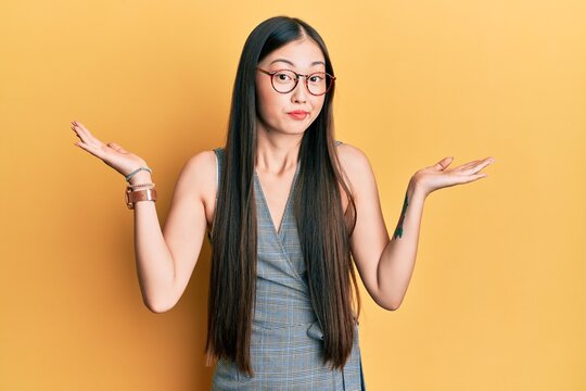 Young chinese woman wearing business dress and glasses clueless and confused with open arms, no idea and doubtful face.
