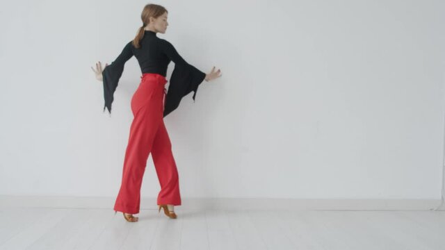Attractive girl dances ballroom dancing in front of a mirror in a bright white hall. A professional ballroom dancer trains in a choreographic hall.