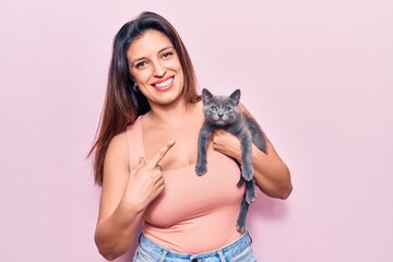 Young beautiful latin woman holding cat smiling happy pointing with hand and finger