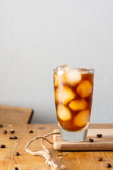 Cold refreshing iced coffee in a glass on a wooden board close-up, cocoa beans are scattered on the table
