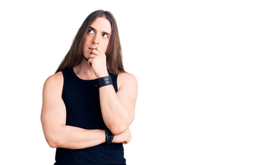 Young adult man with long hair wearing goth style with black clothes with hand on chin thinking about question, pensive expression. smiling and thoughtful face. doubt concept.