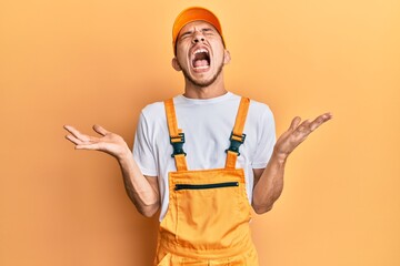 Hispanic young man wearing handyman uniform celebrating mad and crazy for success with arms raised and closed eyes screaming excited. winner concept