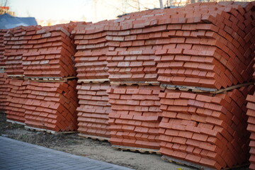 Pile of pallets with red bricks on city street. Building materials on construction site outdoor. Concept of constructing buildings.