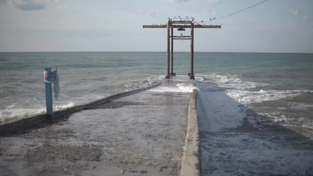 A sea storm with strong waves crushing against the concrete pier.