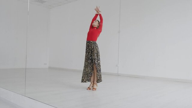 Attractive girl dances ballroom dancing in front of a mirror in a bright white hall. A professional ballroom dancer trains in a choreographic hall.