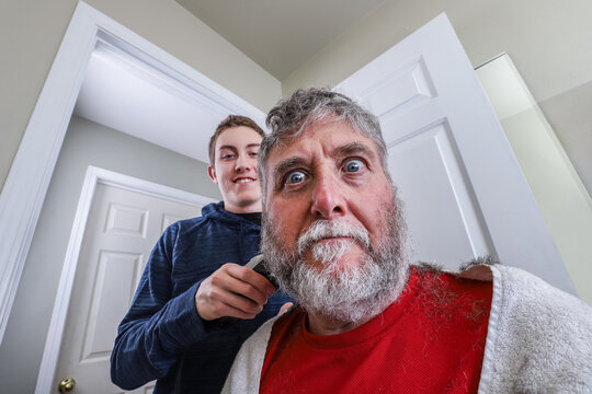 Senior Man With A Beard Getting A Haircut From His Teenage Son