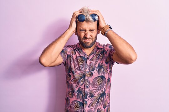 Handsome blond man on vacation wearing casual shirt and sunglasses over pink background suffering from headache desperate and stressed because pain and migraine. Hands on head.