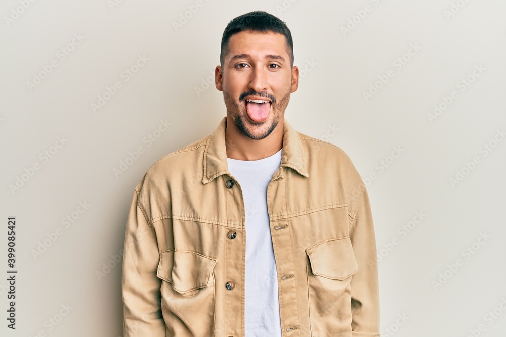 Sticker handsome man with tattoos wearing casual brown denim jacket sticking tongue out happy with funny exp