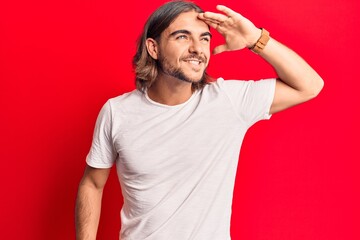 Fototapeta premium Young handsome man wearing casual clothes very happy and smiling looking far away with hand over head. searching concept.