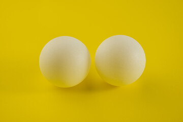 Two white tennis balls lie on a yellow trending background.