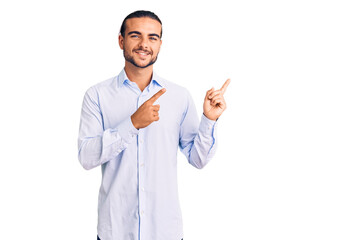 Young handsome man wearing business clothes smiling and looking at the camera pointing with two hands and fingers to the side.