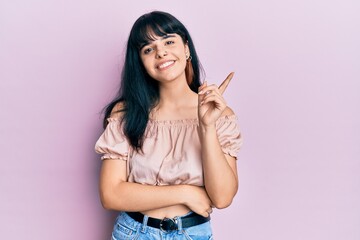 Young hispanic girl wearing casual clothes with a big smile on face, pointing with hand and finger to the side looking at the camera.