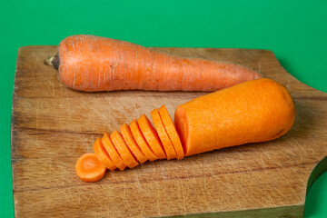 Carrots on a green background. Healthy eating. Sliced carrots next to whole carrots on wooden board