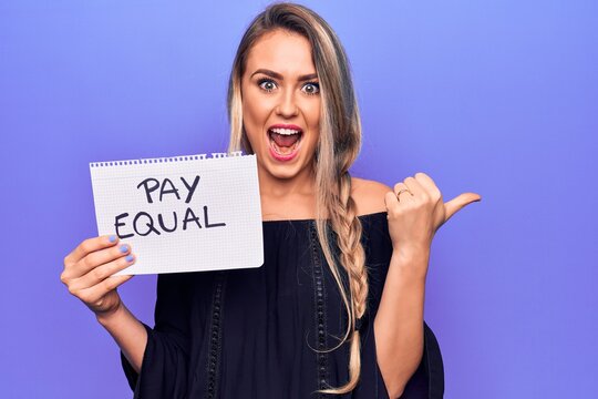 Beautiful blonde woman asking for equality economy holding paper with pay equal message pointing thumb up to the side smiling happy with open mouth