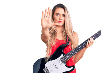 Young beautiful blonde woman playing electric guitar with open hand doing stop sign with serious and confident expression, defense gesture