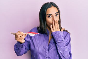 Young brunette woman eating sushi using chopsticks covering mouth with hand, shocked and afraid for...